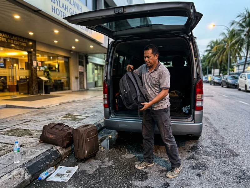 A driver-guide loading bags into the van outside a Kuala Lumpur hotel before dawn